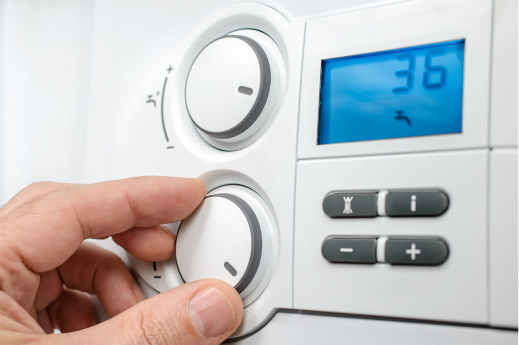 a hand adjusting a dial on a modern combi boiler would benefit from a guide to your combi