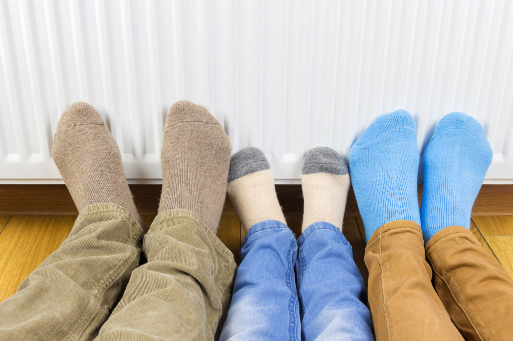 three pairs of feet in front of a radiator making the most out of heating your home