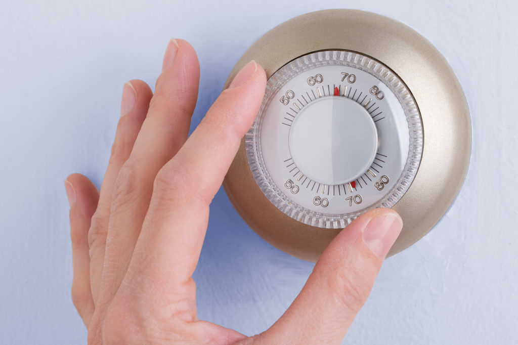 a hand adjusting an old-fashioned room thermostat