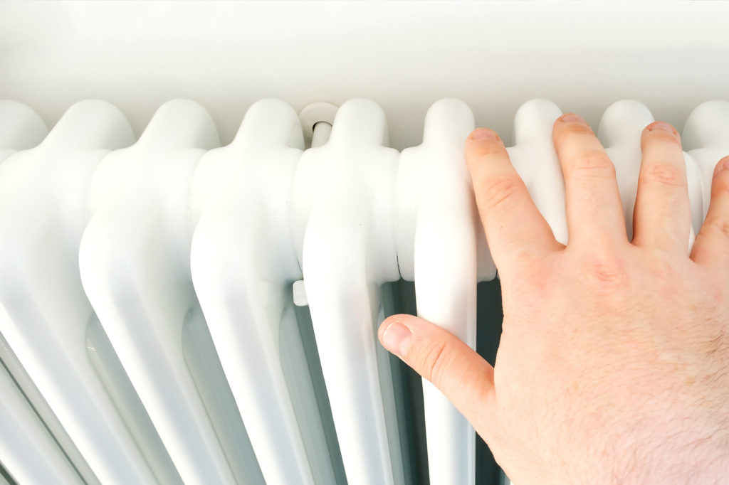 A hand on the radiator showing how to check your heating in the summer before you need it in the winter