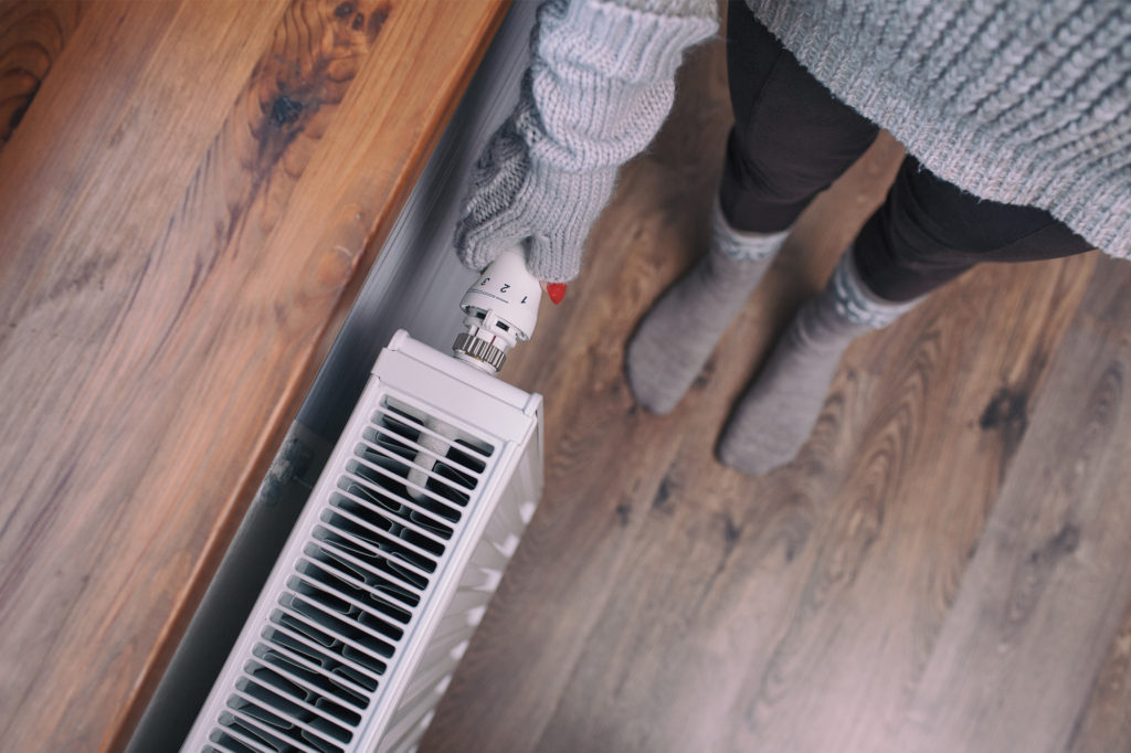 a woman checking her radiator thermostat because her heating is on but the radiator is cold