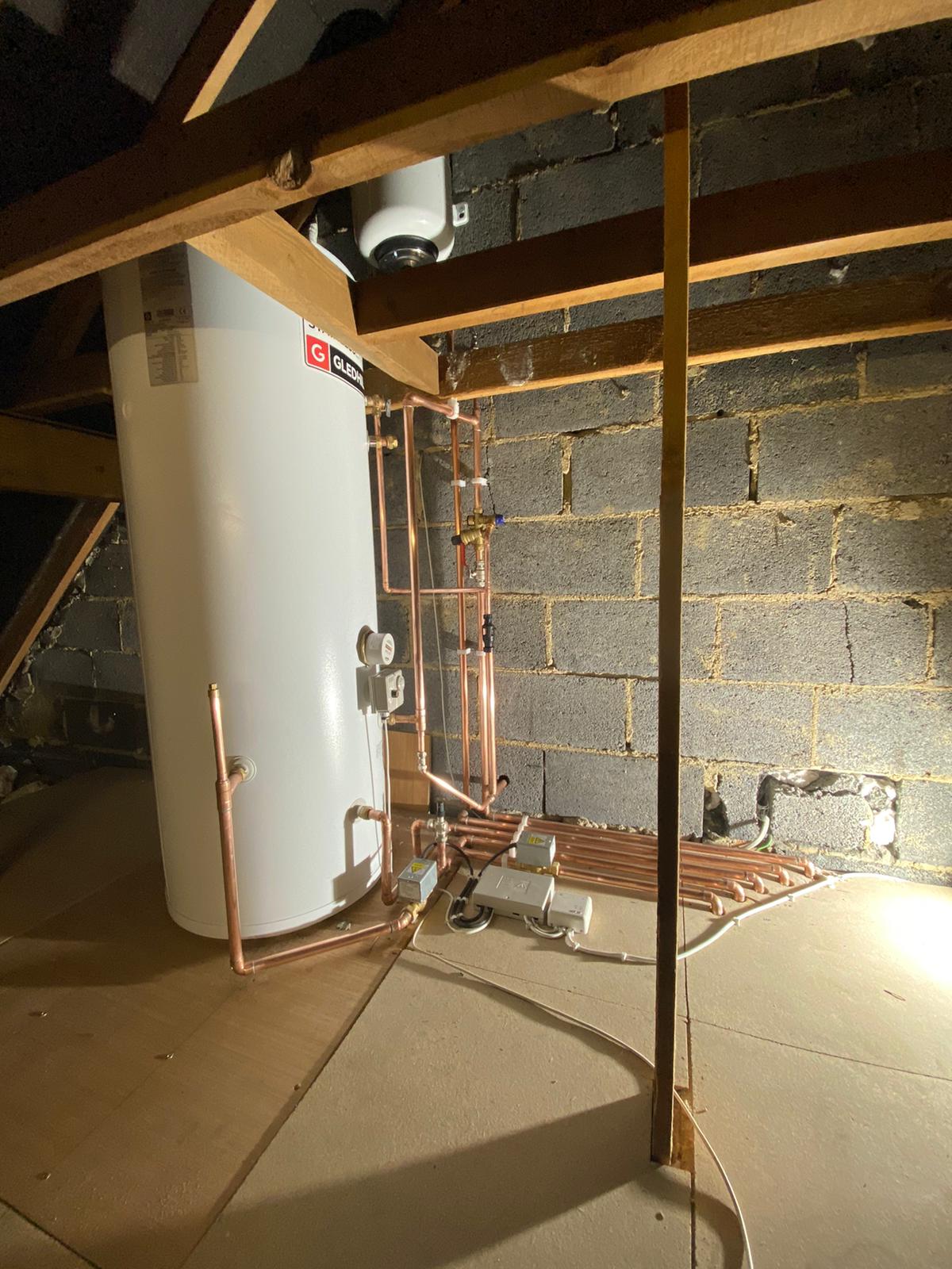 unvented hot water cylinder with exposed pipework and components in loft space.