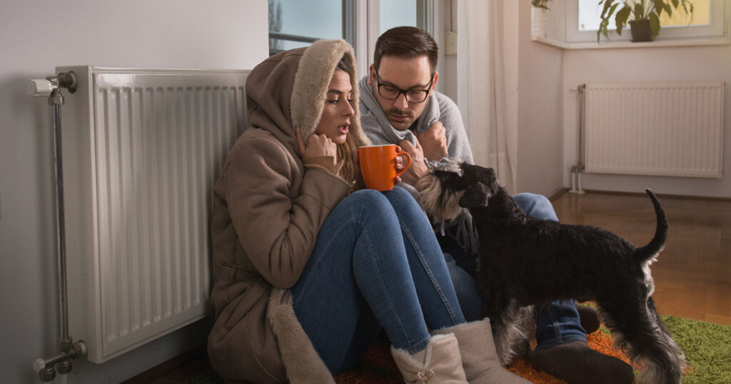 freezing first home couple sitting under blankets by a radiator