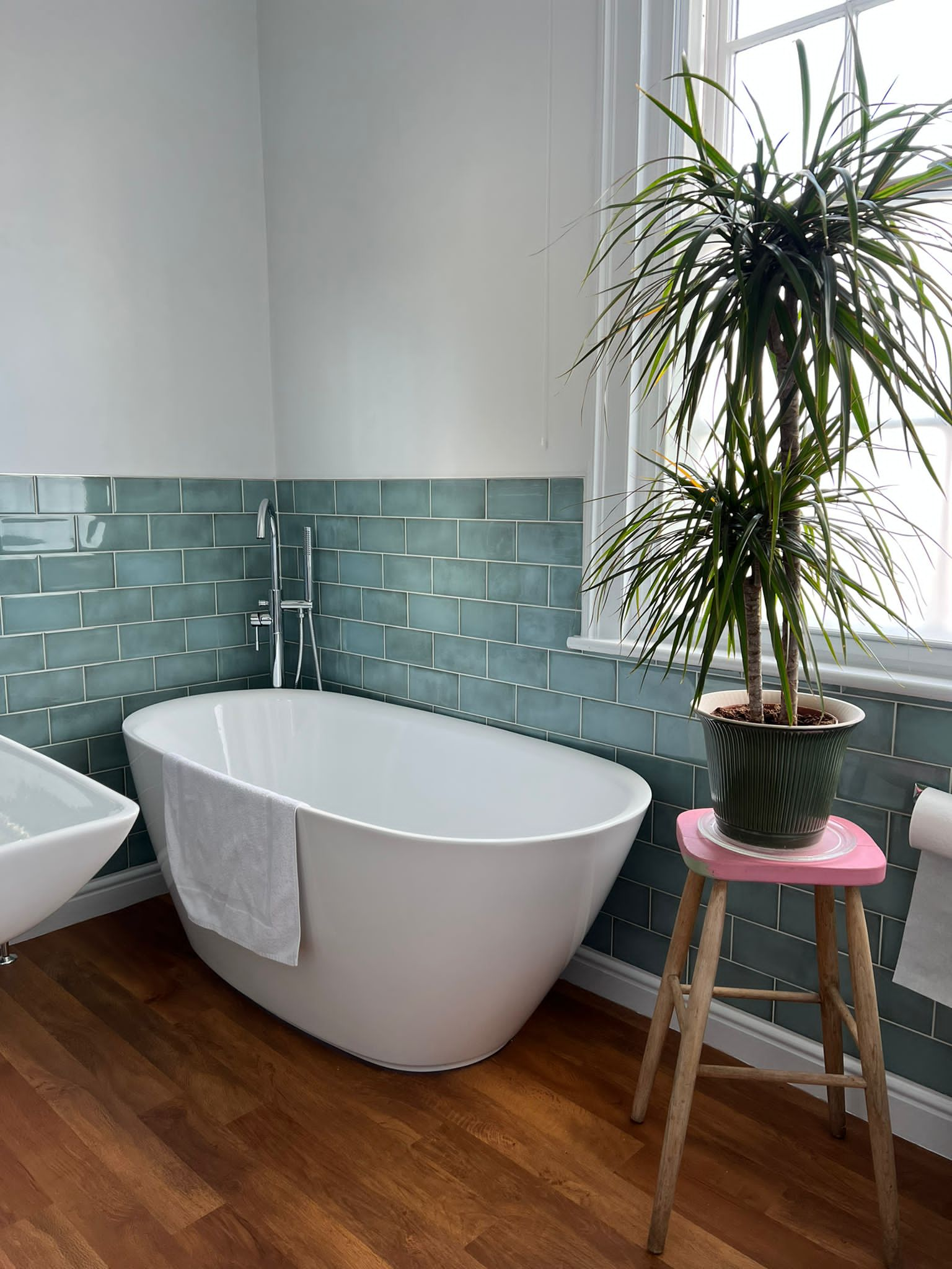 uneven bathroom floor showing view from bathroom door of bath and taps and stool with bathroom plant.