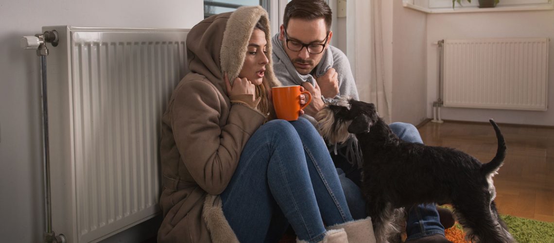 freezing first home couple sitting under blankets by a radiator