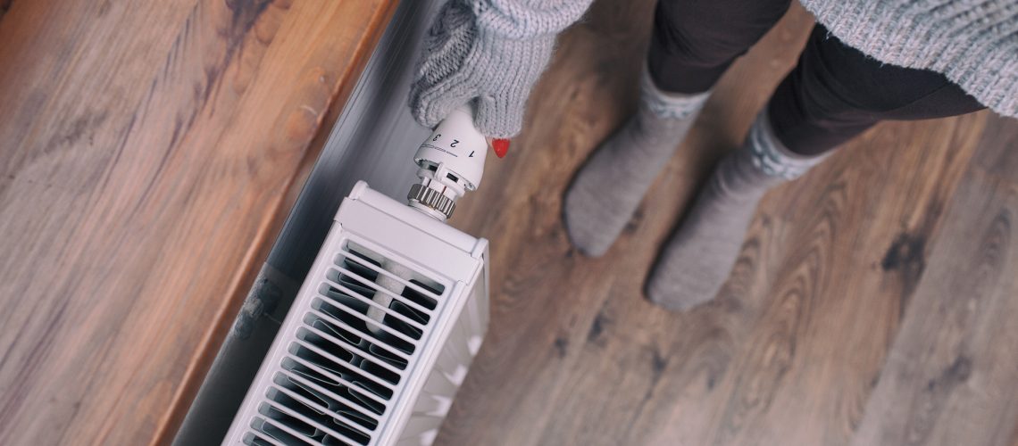 a woman checking her radiator thermostat because her heating is on but the radiator is cold