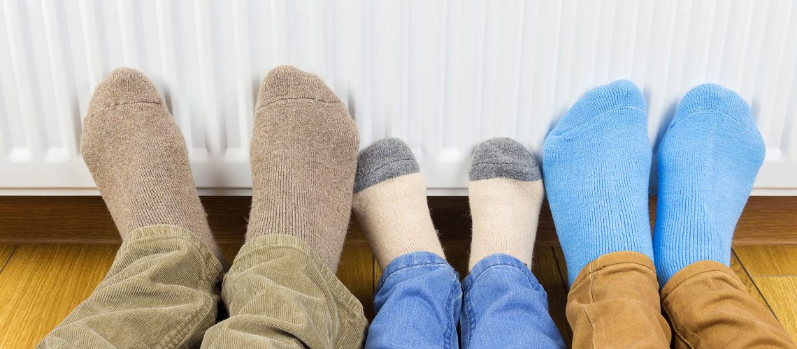 three pairs of feet in front of a radiator making the most out of heating your home