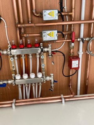 retro-fit underfloor heating manifold and heating pipework mounted on plywood in cupboard