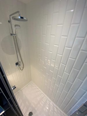 kitchen to bedroom conversion inside shower cubicle with large pan head shower and white vertical brick tiling