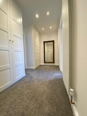 kitchen to bedroom conversion walk in wardrobe with grey carpet and vertical designer radiator and full length mirror