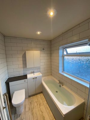 full bathroom suite with vanity cupboard and tessellating floor to ceiling white tiles