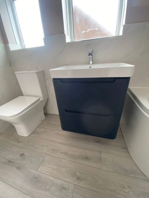 Bathroom refresh image of floating sink and cupboard unit in black and white fixed to wall under window in between bath and toilet..