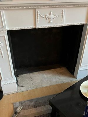 Stove in a fireplace project showing existing white fireplace with black builders opening