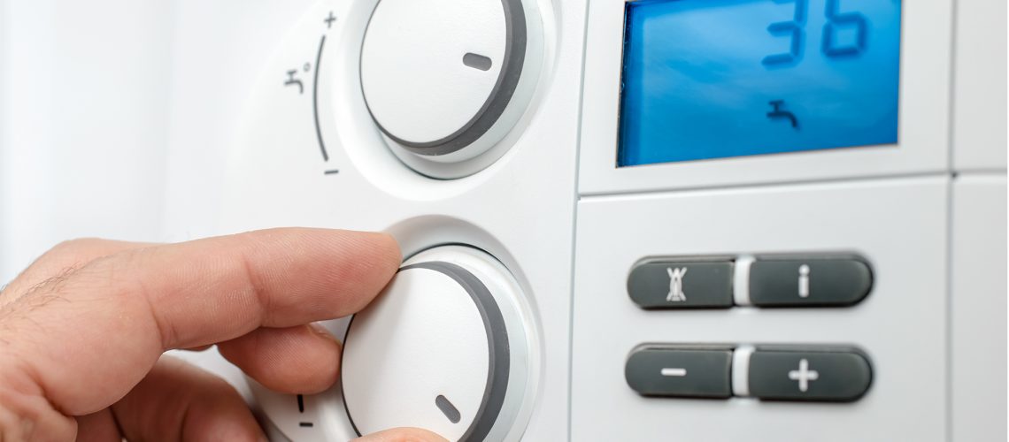 a hand adjusting a dial on a modern combi boiler would benefit from a guide to your combi