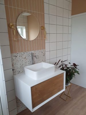 Straight swap bathroom window view of vanity unit complete, comprising of a white and wood effect cupboard and sink mounted on top with mono-mixer tap. 2 types of tiles and mirror with wall mounted pendant lighting.