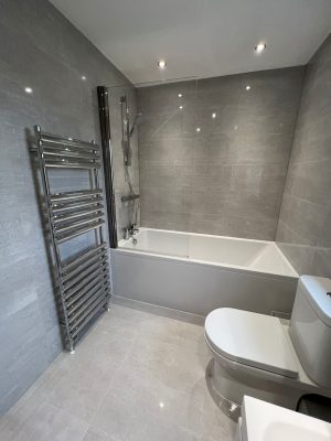 bathroom and ensuite project showing bathroom toilet and large towel rail. Bath has thermostatic shower over bath and glass shower curtain