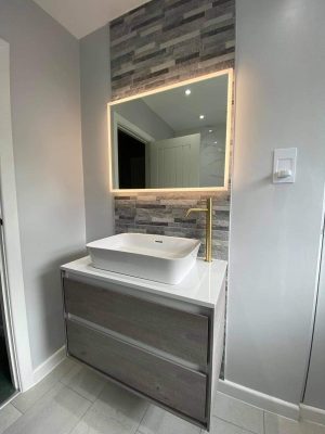 small bathroom renovation completed vanity unit with column of tiles and back lit mirror.