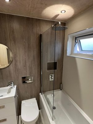 compact bathroom suite furniture comprising of a round mirror, floating two drawer vanity unit and compact toilet with hidden cistern and rain shower head over bath with glass shower screen