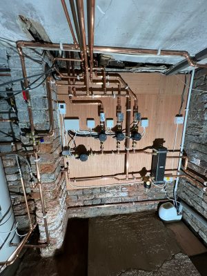 convert offices into a house project shows all controls and pipework on plywood covered cellar wall which includes three heating circuits and one hot water circuit, each one using a pump and motorised valve controlled by a remote thermostat. Heating flow and returns connect to low loss header.