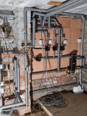 convert offices into a house project shows all controls and pipework on plywood covered cellar wall which includes three heating circuits and one hot water circuit, each one using a pump and motorised valve controlled by a remote thermostat. Heating flow and returns connect to low loss header. All water pipes are lagged