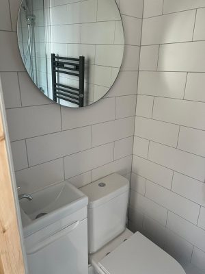 Create an ensuite with tiled walls throughout and large round mirror above toilet and basin