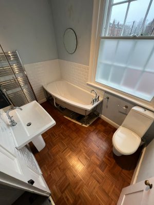 uneven bathroom floor shows existing bathroom suite with toilet bath and basin in view