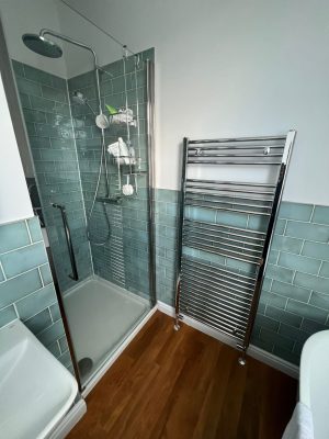 uneven bathroom floor showing new shower cubicle installation and towel rail and green gloss bathroom tiles