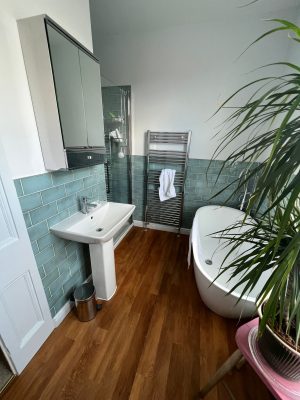 uneven bathroom floor showing new level flooring, basin, bath and taps, towel rail, shower cubicle and green gloss bathroom tiles