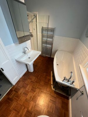 uneven bathroom floor showing existing parquet flooring, bath, sink and inset shower cubicle