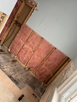 uneven bathroom floor showing existing floorboards in bath corner and exposed wall insulation before tile installation